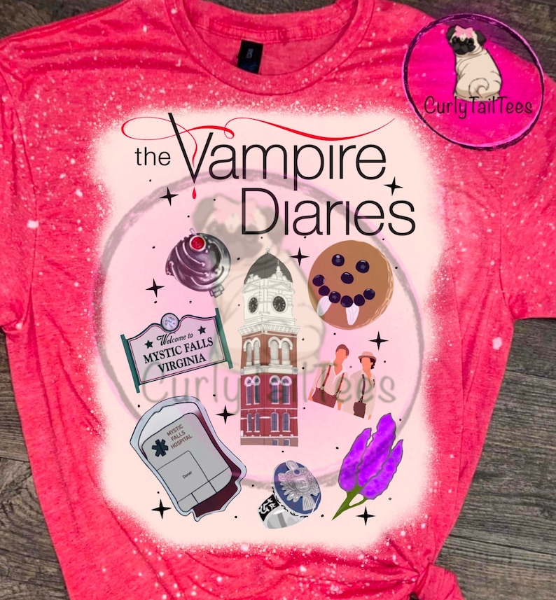 May include: A red t-shirt with a graphic design featuring elements from "The Vampire Diaries." The design includes the show's title, a clock tower, a sign that says "Welcome to Mystic Falls Virginia," and other related illustrations. The shirt has a bleached effect.