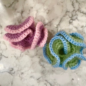 May include: Two crocheted flower shapes, one in pink and purple and the other in green and blue.