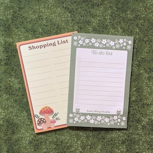 Puede incluir: Dos blocs de notas con ilustraciones florales y de setas. Uno tiene el texto "Shopping List" y el otro "To do list". El bloc de notas "Shopping List" tiene un borde melocotón y un gráfico de setas. El bloc de notas "To do list" tiene un borde verde y detalles florales.