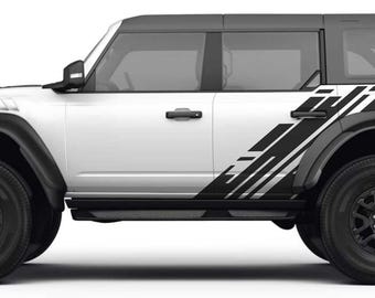 May include: White Ford Bronco with black side graphics. The graphics are a geometric pattern of black and white lines. The vehicle has black wheels and tires.