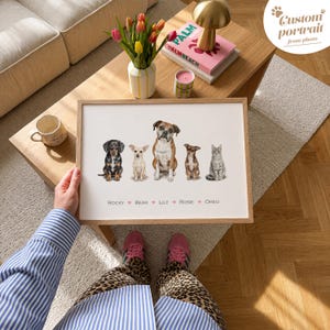 May include: A framed print featuring a watercolor-style illustration of five pets: a black and tan dachshund, a cream chihuahua, a brown and white boxer, a small brown dog, and a grey tabby cat. Below the pets, the names Rocky, Bear, Lily, Rosie, and Oreo are printed in black text separated by small pink hearts.