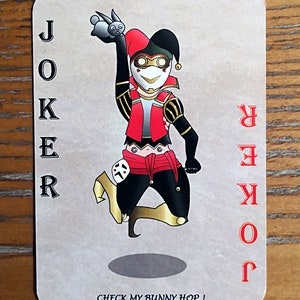 May include: A playing card with a joker illustration. The joker is dressed in a red and black jester costume and is holding a small white rabbit. The card is beige with red text that reads "JOKER" and "CHECK MY BUNNY HOP!"