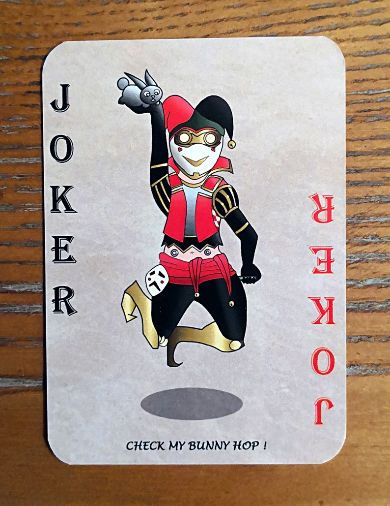 May include: A playing card with a joker illustration. The joker is dressed in a red and black jester costume and is holding a small white rabbit. The card is beige with red text that reads "JOKER" and "CHECK MY BUNNY HOP!"