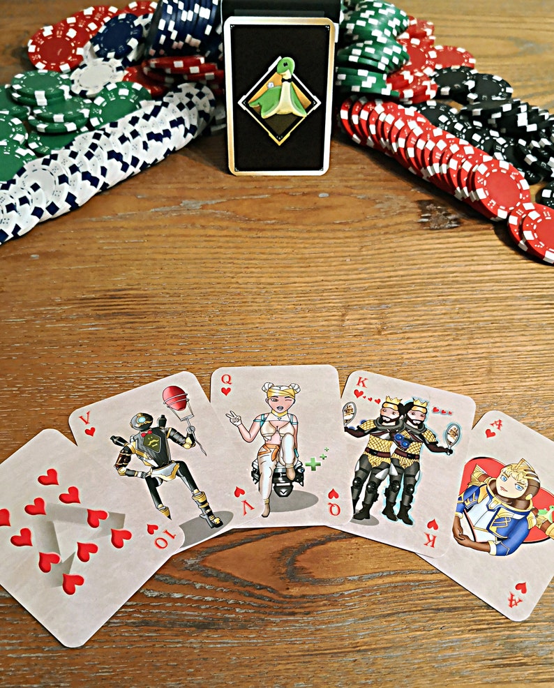 May include: A set of playing cards featuring characters from the video game Apex Legends. The cards are arranged in a semi-circle on a wooden table. The cards are all hearts and include a 10, Jack, Queen, King, and Ace.