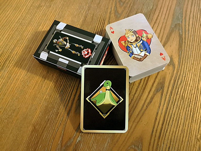 May include: Three playing cards, one with a black background and a green dinosaur wearing a bow tie, one with a brown background and a cartoon character wearing a blue and gold outfit, and one with a black and white background with a robot.
