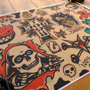 May include: A tan poster with tattoo-style illustrations. Designs include a flaming skull, a cross, a hand, and the text "100% Skateboards". The artwork is in red, black, blue, and gold.