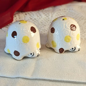 Puede incluir: Dos saleros y pimenteros de cerámica blanca con lunares marrones y amarillos. Los saleros tienen forma de cúpula con fondo redondeado.