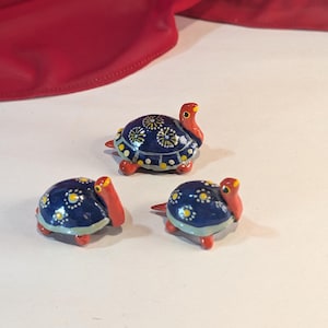 May include: Three small ceramic turtle figurines with blue and white painted shells and red heads. The turtles are painted with yellow flower designs.