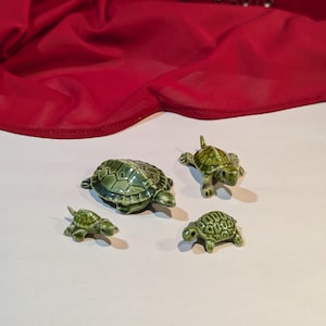 May include: Four green ceramic turtle figurines of varying sizes. The turtles are arranged on a white surface.