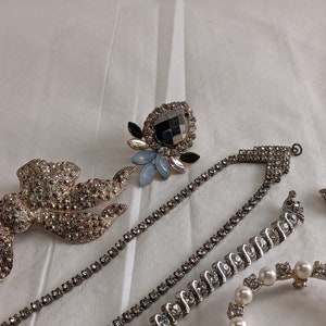 May include: A collection of rhinestone jewellery pieces, including a brooch, a necklace, and a bracelet. The jewellery is silver-toned and features clear and black rhinestones.