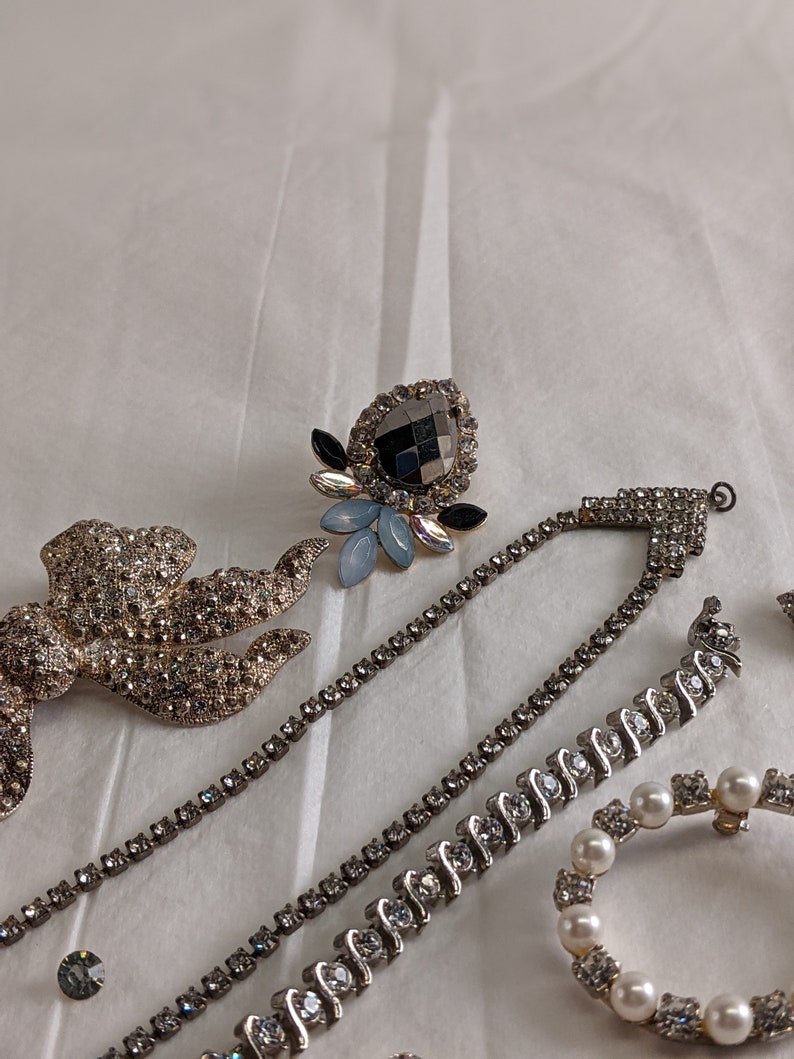 May include: A collection of rhinestone jewellery pieces, including a brooch, a necklace, and a bracelet. The jewellery is silver-toned and features clear and black rhinestones.