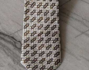 May include: A white silk tie with a geometric pattern of brown and black ovals. The pattern is repeated throughout the tie.