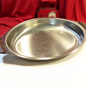 Puede incluir: Una bandeja ovalada de servir plateada con dos asas de madera. La bandeja está vacía y tiene una superficie brillante y reflectante.