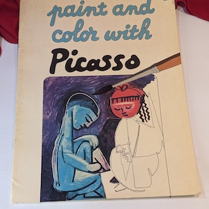 Peut inclure: Une couverture de livre de coloriage vintage représentant une illustration en noir et blanc de deux personnages. La couverture porte le texte "paint and color with Picasso" en lettres bleues et noires.