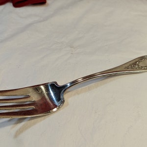 May include: A silver fork with an ornate handle. The handle features a heart-shaped design with floral details.
