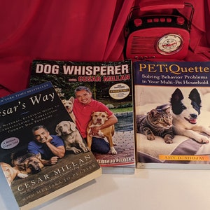 May include: Three dog training books with Cesar Millan's name on the cover. The books are titled "Cesar's Way", "Dog Whisperer with Cesar Millan", and "PETiQuette Solving Behaviour Problems in Your Multi-Pet Household".