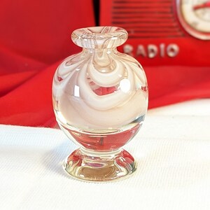 May include: A small, clear glass vase with a white swirl design. The vase has a round body and a flared base.