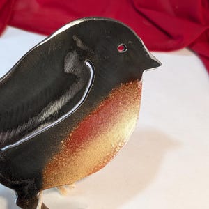May include: A metal sculpture of a robin with a black body, red and gold accents, and a white outline. The robin is standing on a metal base.