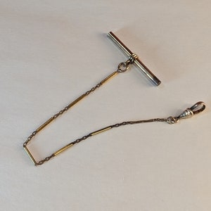 May include: A gold pocket watch chain with a silver T-bar and a silver clasp.