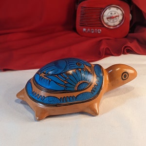 Può includere: Una statuetta di tartaruga in ceramica dipinta a mano con motivi floreali blu e arancioni. La tartaruga è marrone e ha un guscio dettagliato.
