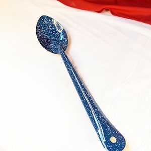 May include: A blue enamel spoon with white speckles. The spoon has a long handle and a rounded bowl.