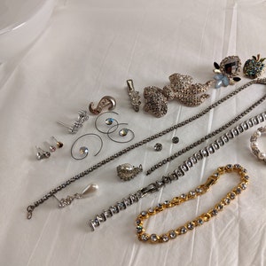 May include: A collection of silver and gold tone jewellery featuring rhinestones, pearls, and a variety of designs. The jewellery includes earrings, necklaces, bracelets, and brooches.