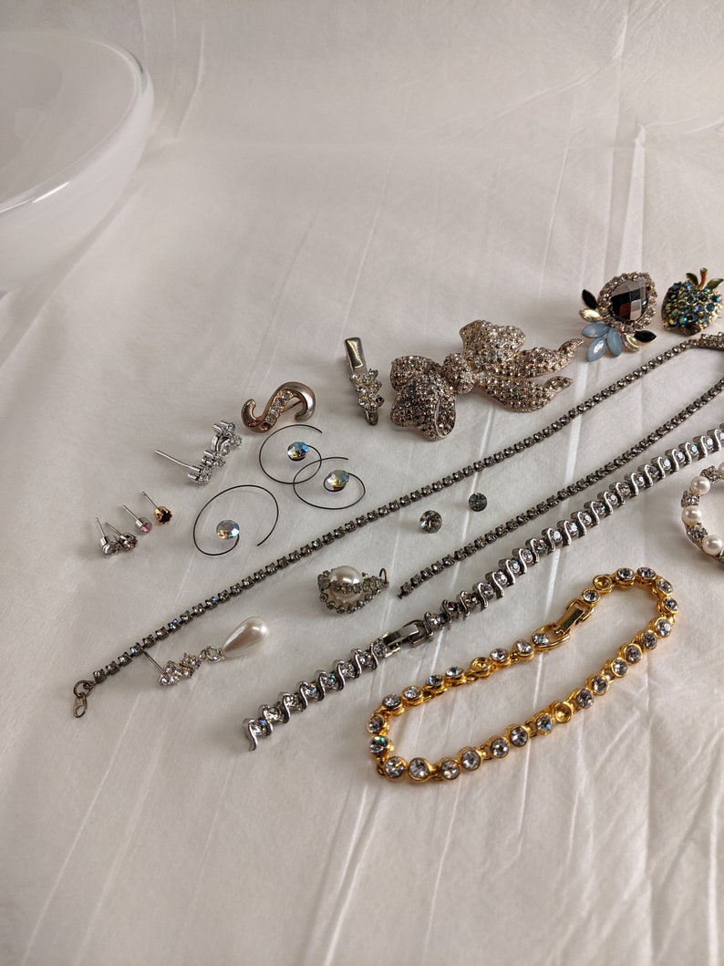 May include: A collection of silver and gold tone jewellery featuring rhinestones, pearls, and a variety of designs. The jewellery includes earrings, necklaces, bracelets, and brooches.