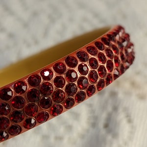 May include: A close-up of a red bangle bracelet with a row of small, red rhinestones.