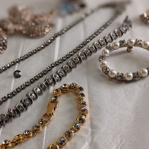May include: A set of three silver and gold necklaces with crystal and pearl accents. The necklaces are arranged on a white surface.