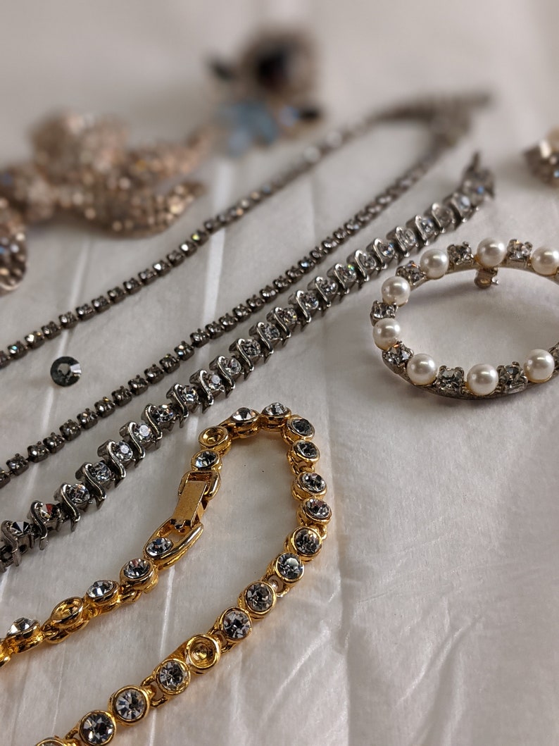 May include: A set of three silver and gold necklaces with crystal and pearl accents. The necklaces are arranged on a white surface.