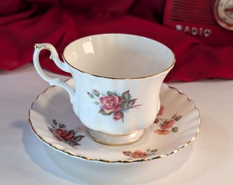 Può includere: Una tazza da tè e un piattino bianchi con un bordo dorato e un motivo floreale con rose rosa.