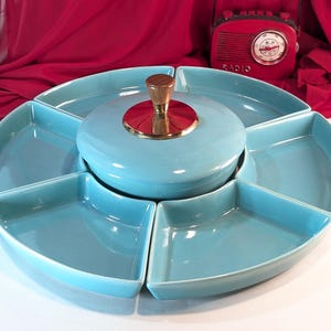 Puede incluir: Un juego de fuentes turquesa vintage con un cuenco central con tapa y seis compartimentos en forma de cuña. La tapa tiene un asa de madera y adornos dorados. Una radio roja vintage está en el fondo.