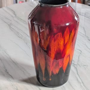 Peut inclure: Un vase en céramique rouge et orange avec une base noire. Le vase a un design unique et abstrait avec des stries orange et jaunes.