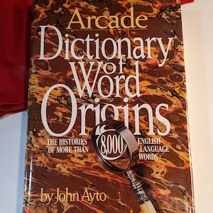 May include: A brown book titled "Arcade Dictionary of Word Origins" with a magnifying glass on the cover. The book features the text "The histories of more than 8,000 English-language words" and "by John Ayto".