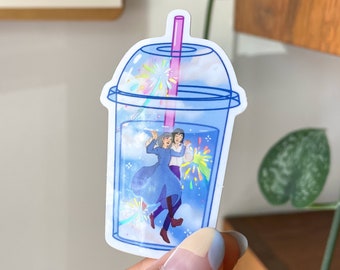 May include: A blue and white plastic cup with a pink straw. Two cartoon figures are inside the cup, floating in a blue liquid with white clouds and colorful fireworks.