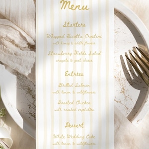 May include: A vertical rectangular menu card featuring a white background with pale yellow vertical stripes and gold cursive text. The menu lists Starters, Entrees, and Dessert, including items like Whipped Ricotta Crostini and Grilled Salmon.