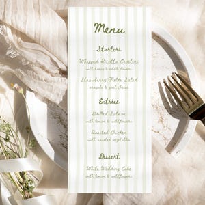 Puede incluir: Una tarjeta de menú vertical con un fondo a rayas verdes y blancas. El menú incluye entrantes, platos principales y postres. Los elementos del menú están escritos en una fuente manuscrita. La tarjeta está sobre un plato blanco con un tenedor dorado.