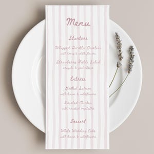 Könnte beinhalten: Eine rechteckige Menükarte mit vertikalen hellrosa Streifen und dunkelrosa Schreibschrift. Das Menü listet Starters, Entrees und Dessert auf, darunter Gerichte wie Whipped Ricotta Crostini und Grilled Salmon. Zwei Zweige getrockneter Lavendel sind sichtbar.