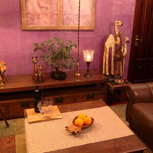 May include: A wooden elephant figurine, two wooden cat figurines, and two wooden giraffe figurines are displayed on a wooden shelf. A wooden table with a bowl of oranges sits in front of the shelf. A brown leather armchair is in the background.