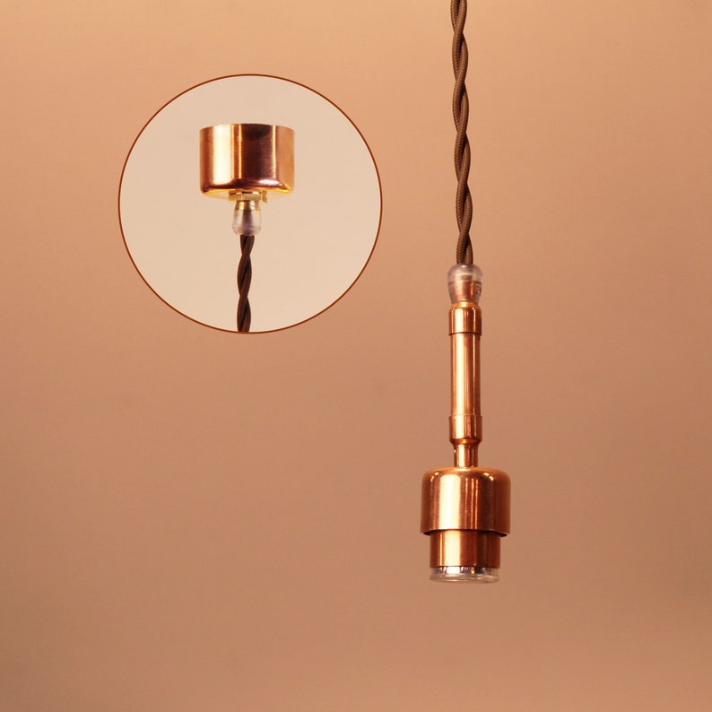 May include: A copper ceiling light fixture with a brown braided cord. The fixture has a simple design with a round base and a cylindrical shade.