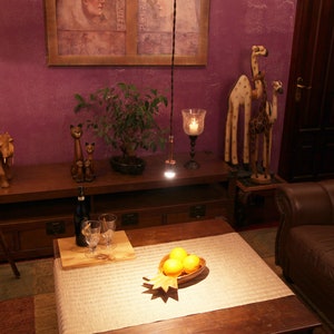 May include: A living room interior with a wooden table, a brown leather armchair, and a wooden tripod lamp with a lampshade. There are wooden animal figurines on the table, including an elephant and giraffes. A potted bonsai tree is on the table. There are three oranges in a wooden bowl on a table with a white tablecloth.