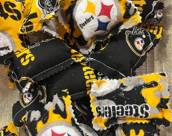 May include: A collection of fabric scraps featuring the Pittsburgh Steelers logo and the word "Steelers". The scraps are in black, yellow, and white with a star design.