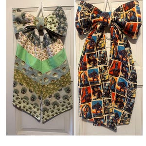 May include: Two large fabric bows with long hanging tails. The left bow features a patchwork of light green and gray fabric with cartoon character prints. The right bow features a vibrant comic book style print with multiple character panels.