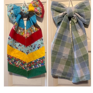 May include: Two fabric bows with long tails. The left bow features a multi-colored patchwork design with various cartoon character prints, red, yellow, and green sections. The right bow has a light blue and sage green plaid pattern.