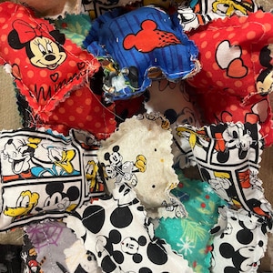 May include: A collection of colorful fabric squares featuring various Disney characters, including Mickey Mouse, Minnie Mouse, Donald Duck, and Goofy. The squares are sewn together to create a patchwork design.