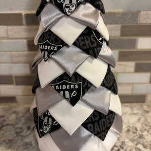 May include: A white, silver, and black fabric Christmas tree with the Raiders logo and the word "Raiders" repeated throughout.
