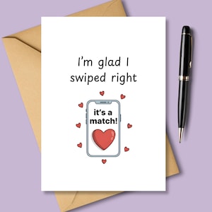 Pode incluir: Um cartão branco com o texto "I'm glad I swiped right" e um smartphone de desenho animado com um coração e as palavras "it's a match!". O cartão é rodeado por pequenos corações vermelhos e está ao lado de uma caneta preta e um envelope castanho.