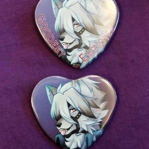 May include: Two heart-shaped buttons with a furry, white wolf-like character with a black collar and a purple background. The text "GOODEST EMPLOYEE" is printed on the button.