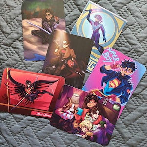 Könnte beinhalten: Eine Sammlung von sechs rechteckigen Kunstdrucken mit Comicfiguren. Die Drucke zeigen Illustrationen von Superhelden in verschiedenen Actionposen und Umgebungen. Die Farbpalette umfasst Rot-, Blau- und Lilatöne, wobei einige Drucke Text wie "Super Boy" und "Red Robin" zeigen.