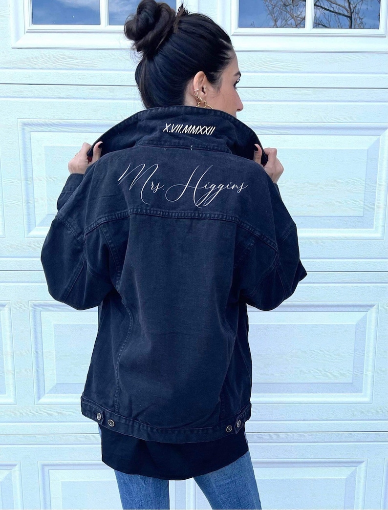 Pu&ograve; includere: Una giacca di jeans nera con il testo "Mrs. Higgins" ricamato sul retro e "XVII.VII.MMXXII" ricamato sul colletto.